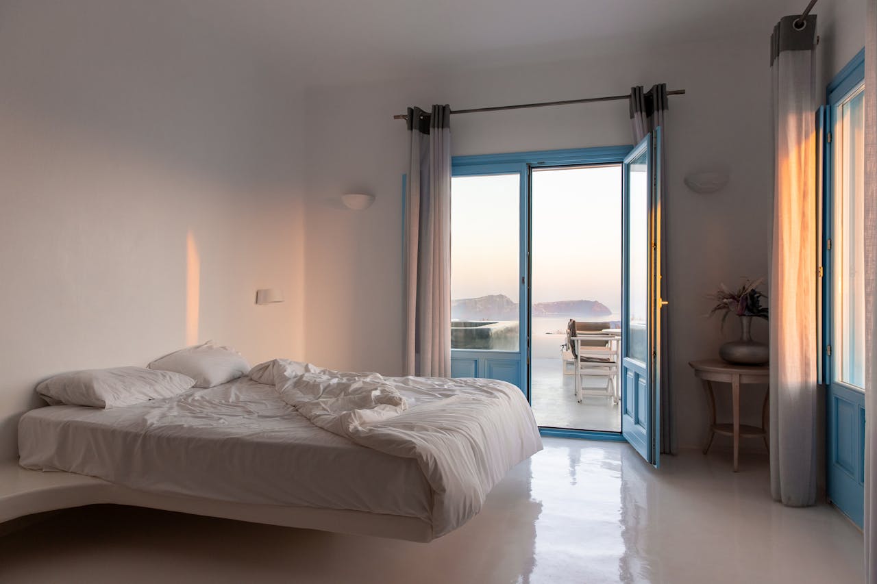 Elegant hotel room with sea view balcony in Akrotiri, featuring modern interior design and sunset glow.